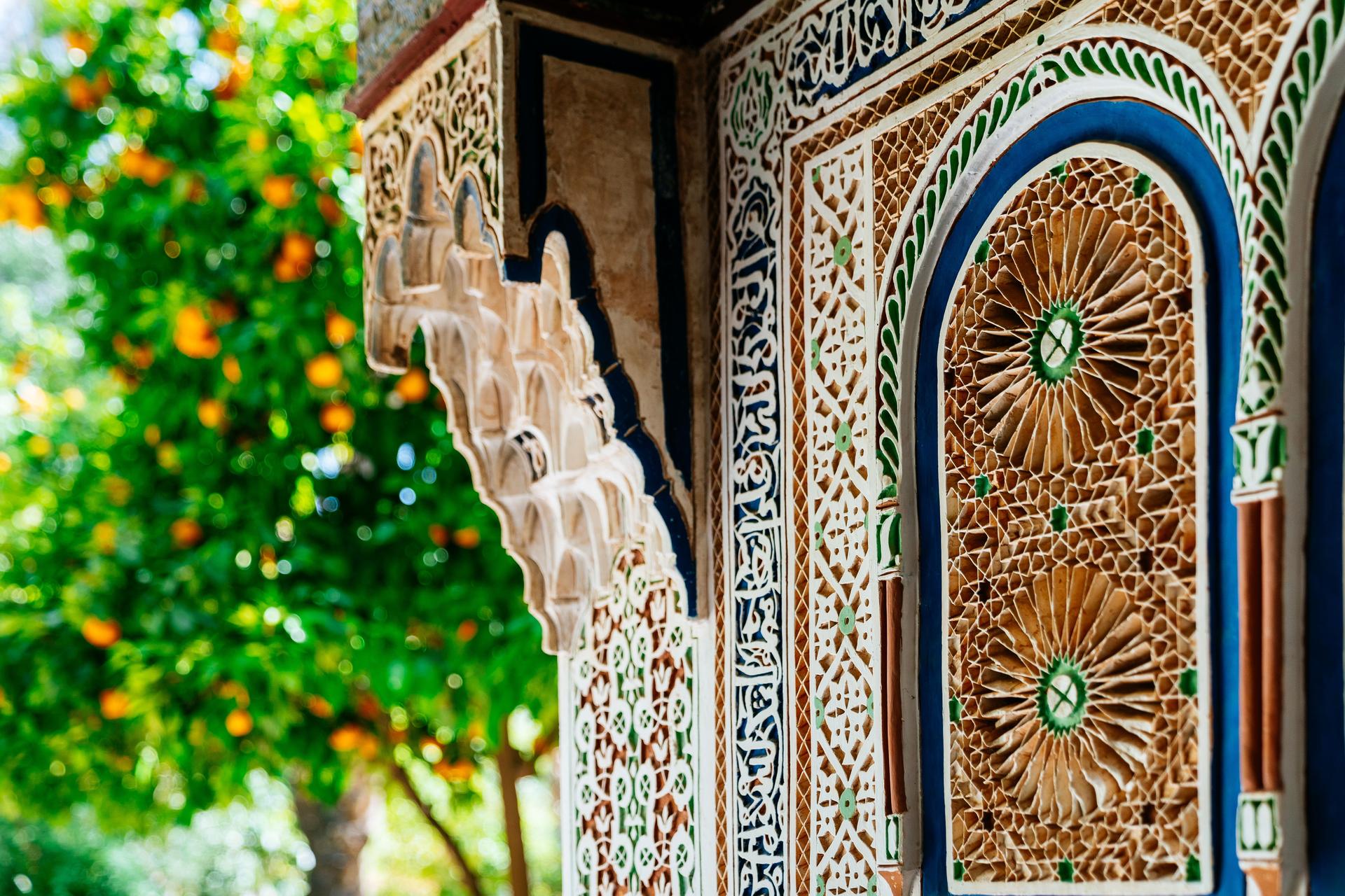 Palais de la Bahia à Marrakech. Le mur du palais, décoré avec des motifs traditionnels marocains, des mosaïques et des inscriptions en arabe. Orangers sur le fond.